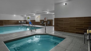 Una piscina interior con agua cristalina, rodeada de suelo de baldosas y detalles de madera.