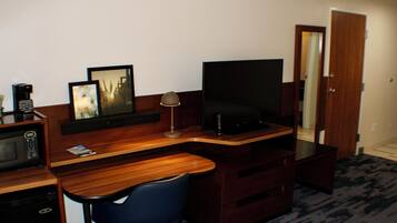A hotel room with a wooden desk, a television, a microwave, a chair, and a mirror.