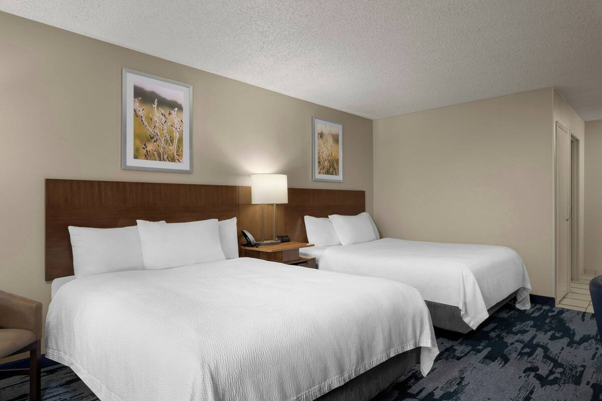 A hotel room with two beds, a nightstand with a lamp, and two framed pictures on the wall.