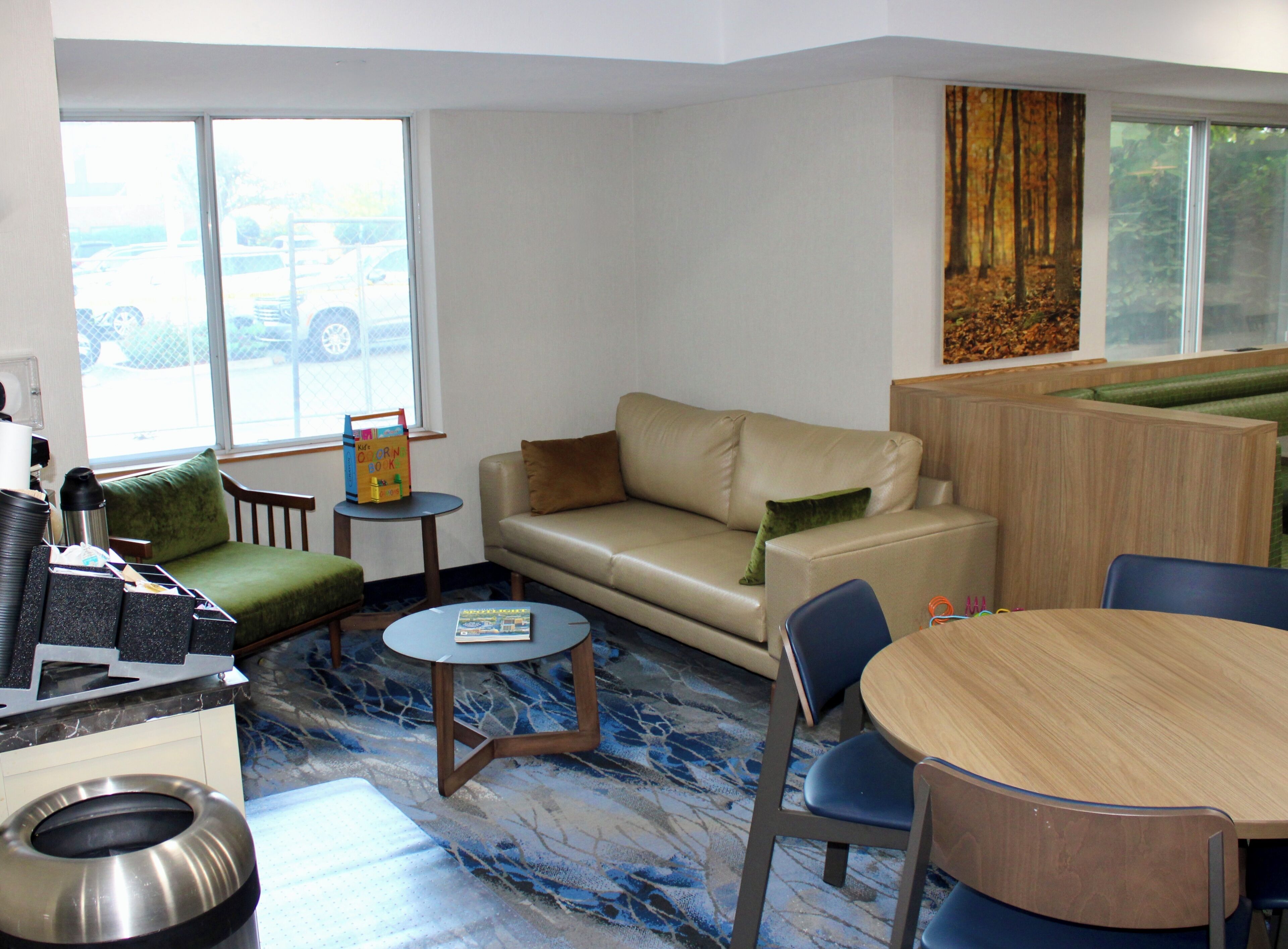 A hotel room with a sofa, a small table, a round table, and a trash bin.