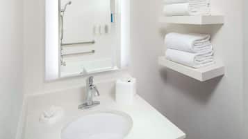 A bathroom with a white sink, a mirror, a towel rack, and a toilet paper holder.