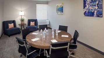Uma sala de conferência com uma mesa redonda, seis cadeiras e um vaso de planta.