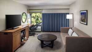 A hotel room with a flat-screen TV, a wooden desk with a microwave, a round coffee table, a sofa, and a large window with curtains. - Hampton Inn Atlanta-Northlake (Atlanta)