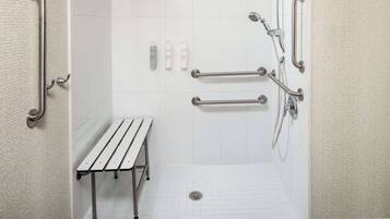 Un baño con paredes de azulejos blancos, un banco y varios pasamanos.
