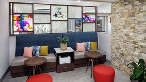 A modern waiting area with a sofa, two red ottomans, a small table with a printer, and a decorative wall with a plant. - Hampton Inn Atlanta-Northlake (Atlanta)