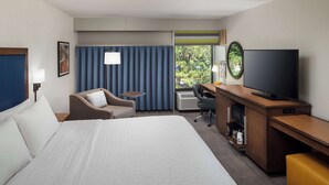 A hotel room with a large bed, a desk with a flat-screen TV, a chair, a small table, and a window with curtains. - Hampton Inn Atlanta-Northlake (Atlanta)
