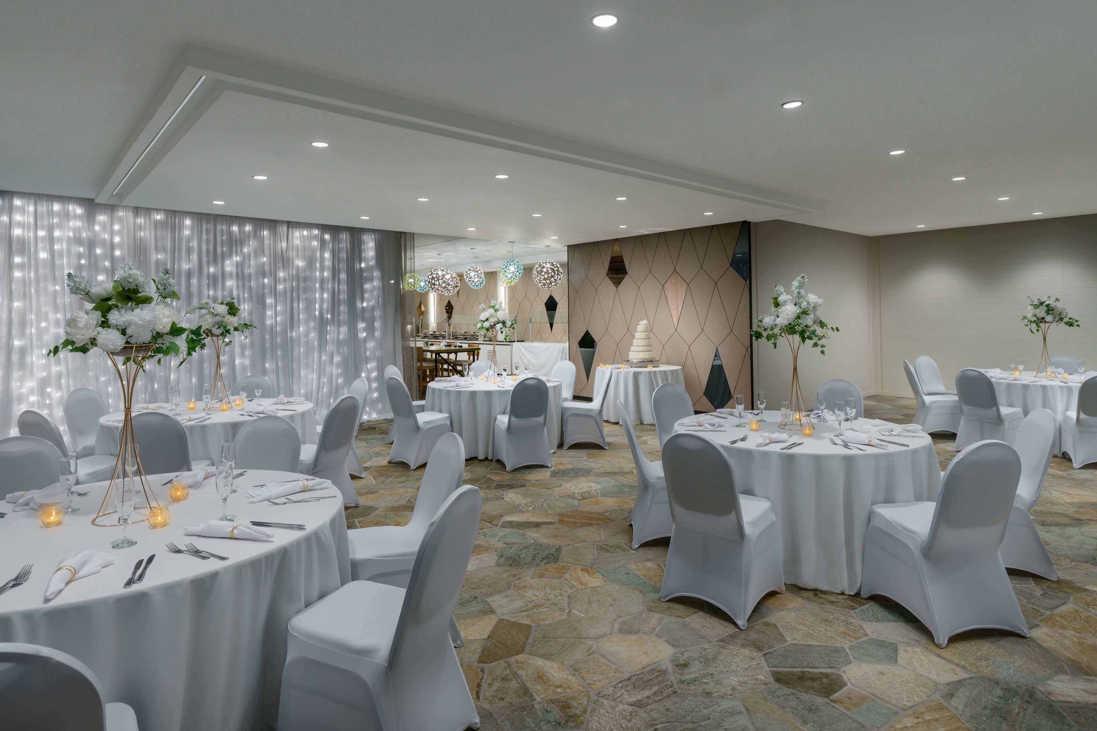 Un salón de banquetes con mesas redondas, sillas blancas y centros de mesa florales.