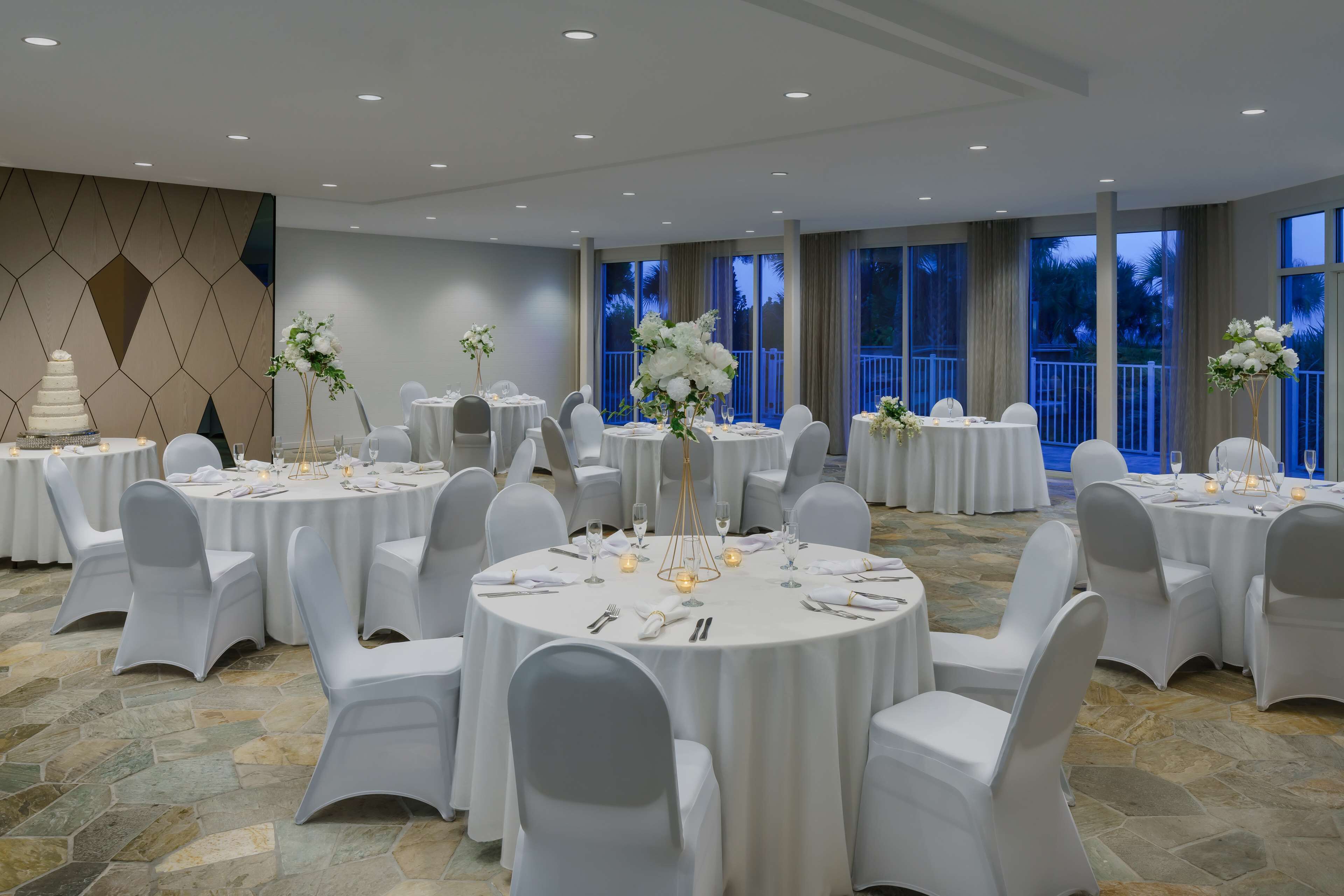 A banquet hall with round tables, white chairs, and floral centerpieces.