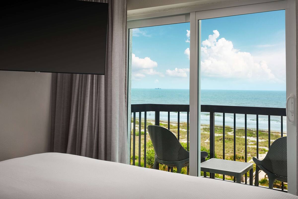 Et hotelværelse med seng, fjernsyn og balkon med stole og bord.