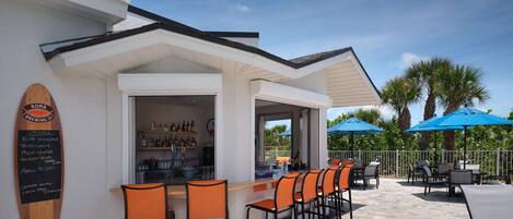 An outdoor bar area with a counter, multiple chairs, and umbrellas.
