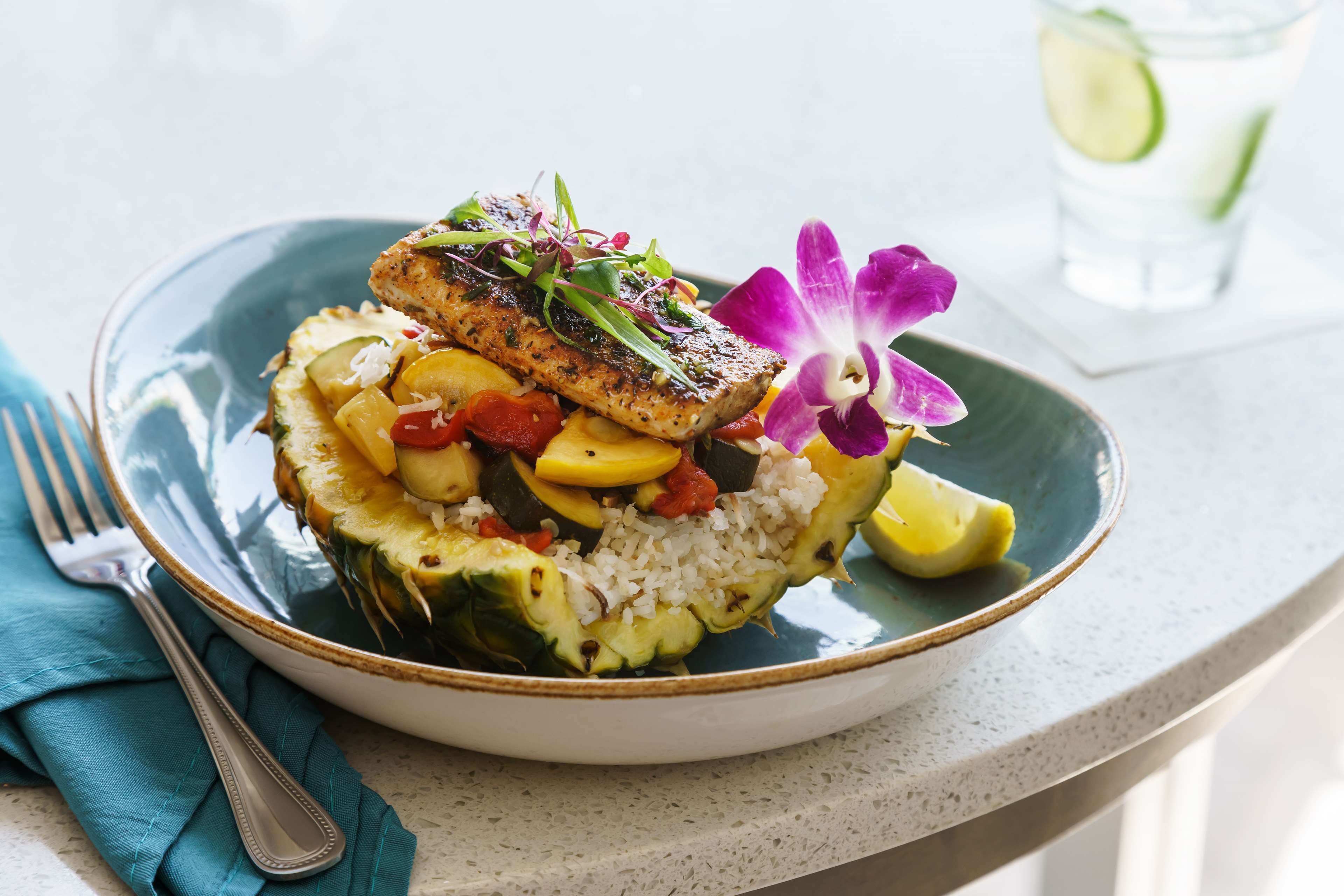 Une assiette contenant un filet de poisson, du riz et des légumes, accompagnée d’une fourchette et d’une serviette.