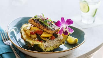 A plate of food with a fish fillet, rice, and vegetables, accompanied by a fork and a napkin.