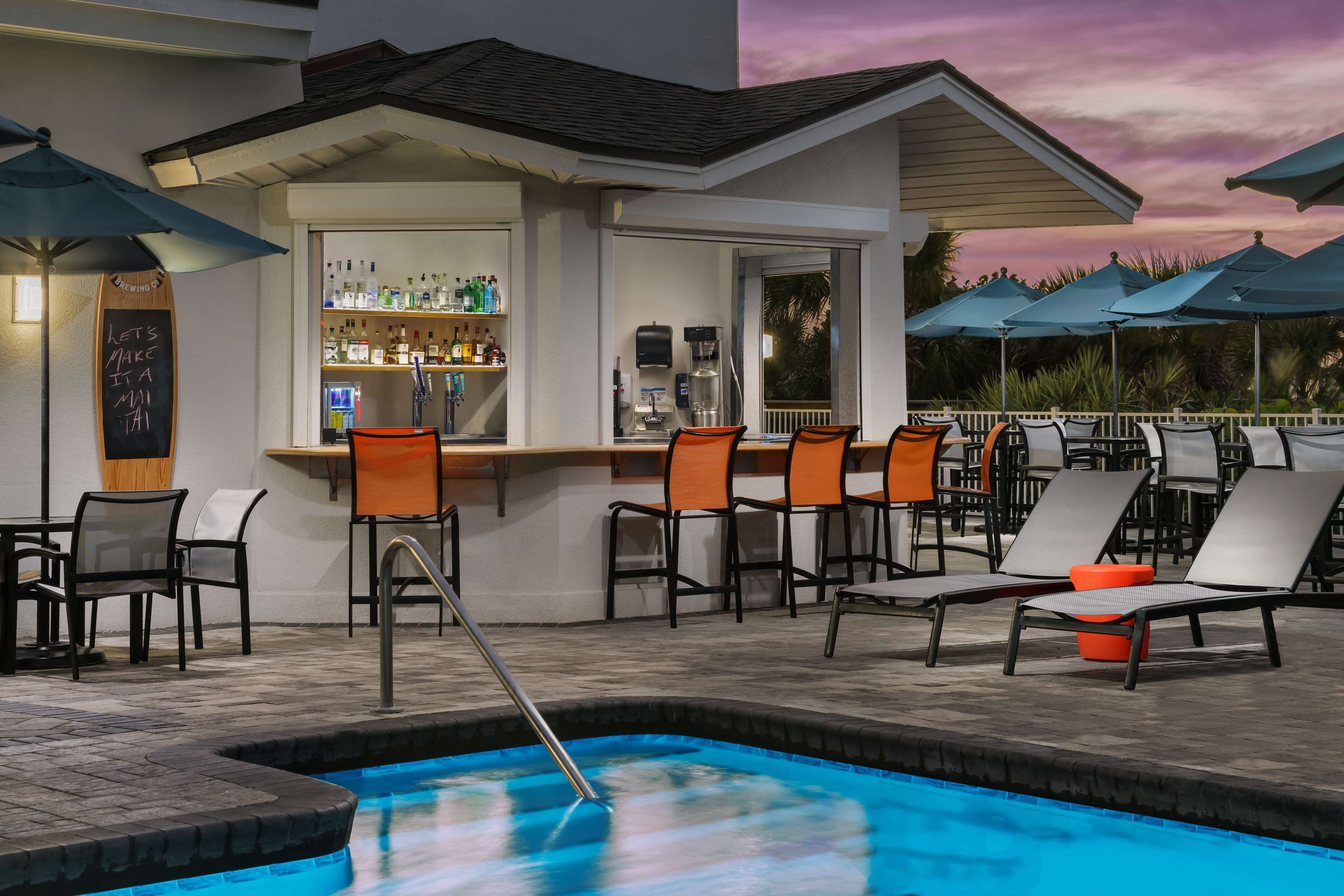 A poolside area with lounge chairs, a bar, and a pool.
