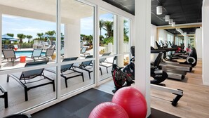 Un gimnasio con equipo de ejercicio, un área de piscina con sillas de descanso y amplias ventanas con vistas al exterior.
