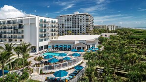 Un hotel con varios pisos, una zona de piscina con sombrillas y vista al océano.