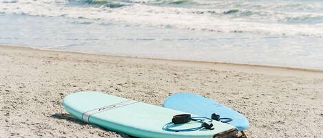 Two surfboards on a sandy beach with the ocean in the background.