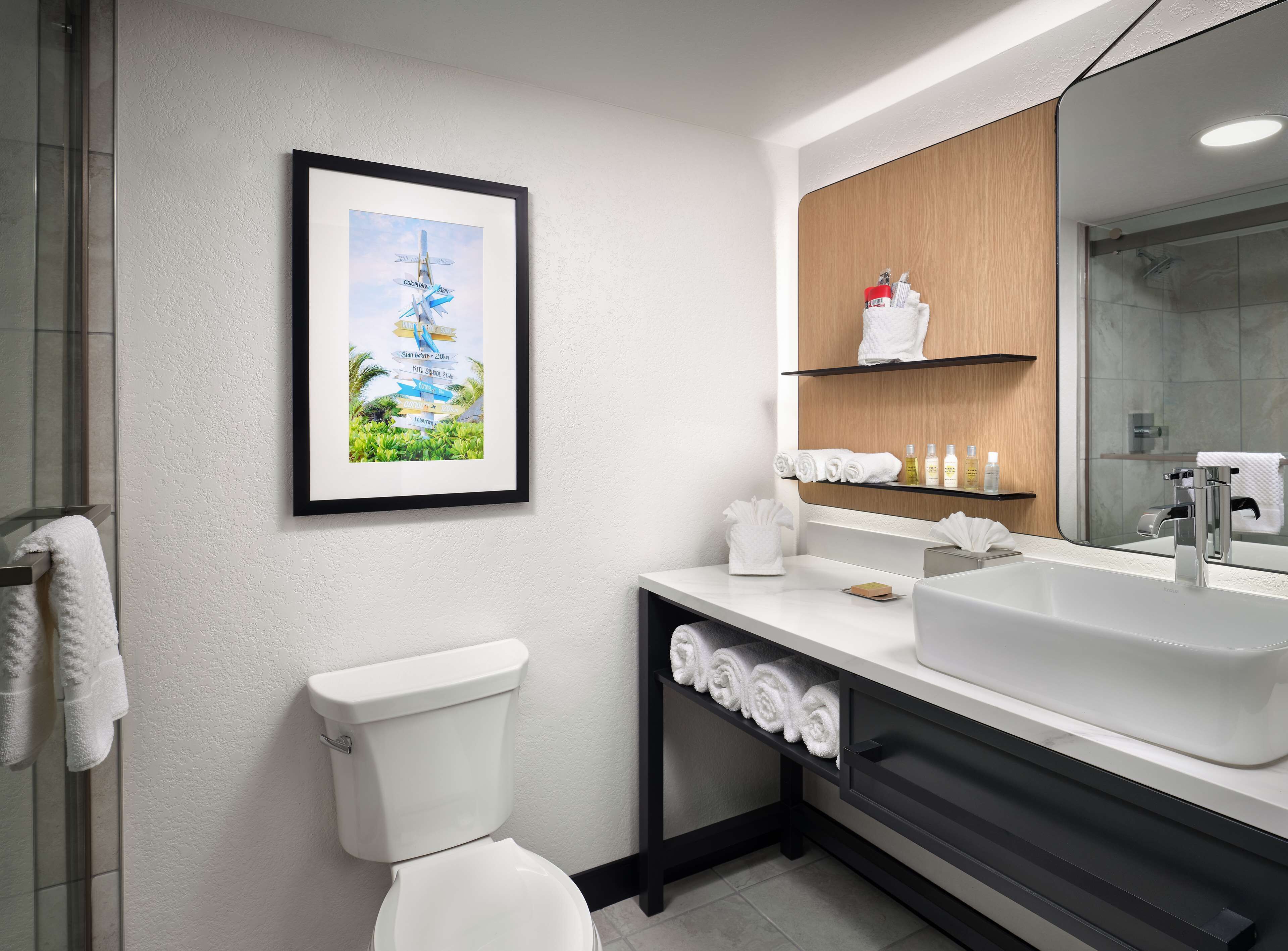 Un baño moderno con inodoro blanco, un lavamanos grande, un espejo y un cuadro con aviones en la pared.