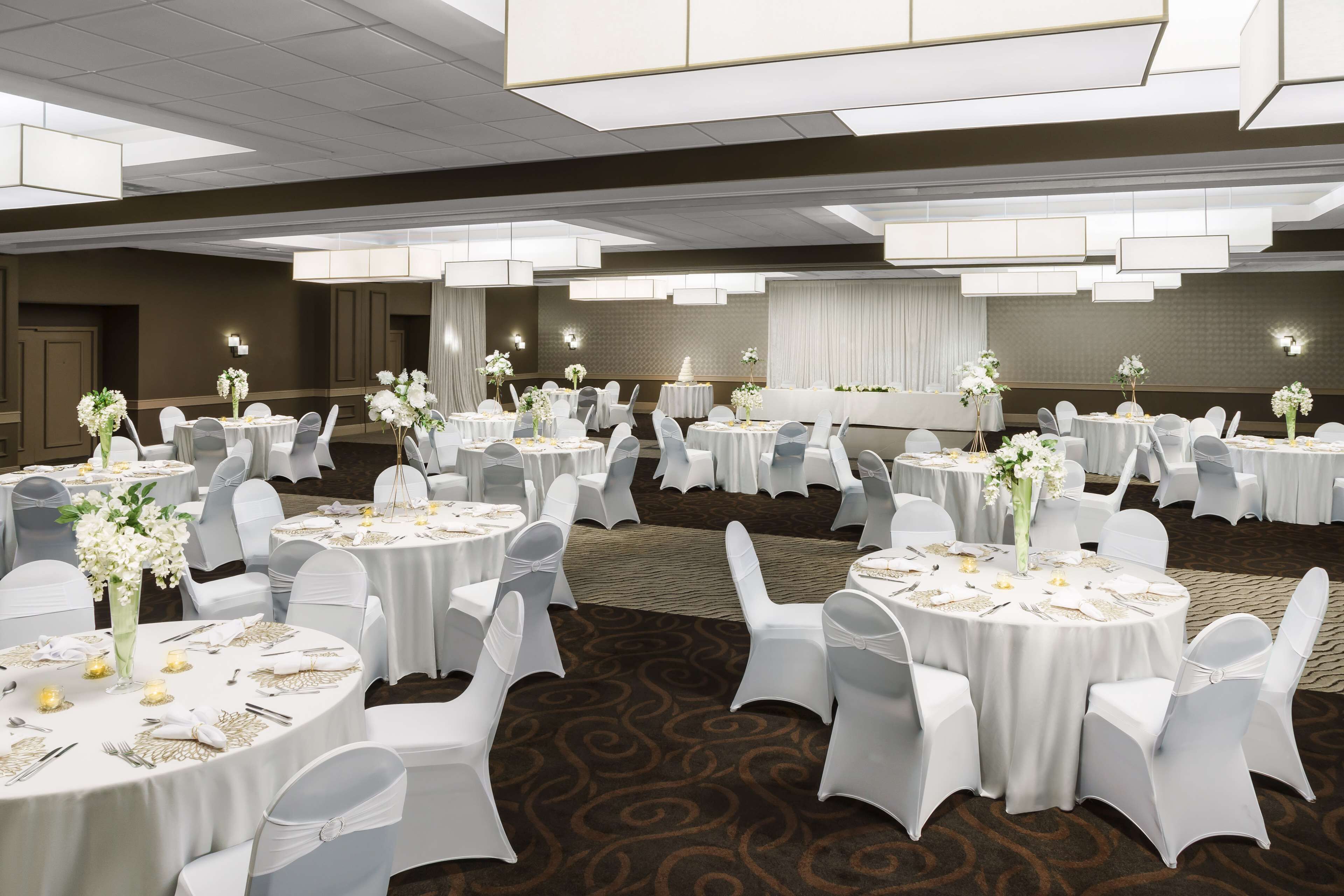 Een balzaal met ronde tafels, witte stoelen en bloemstukken als decoratie.