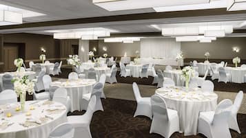 Een balzaal met ronde tafels, witte stoelen en bloemstukken als decoratie.