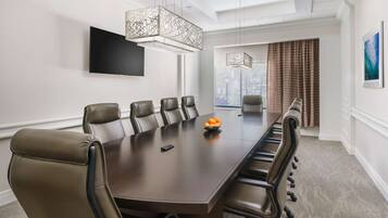 Une salle de conférence avec une longue table, des fauteuils en cuir, un saladier rempli d’oranges et un téléviseur fixé au mur.