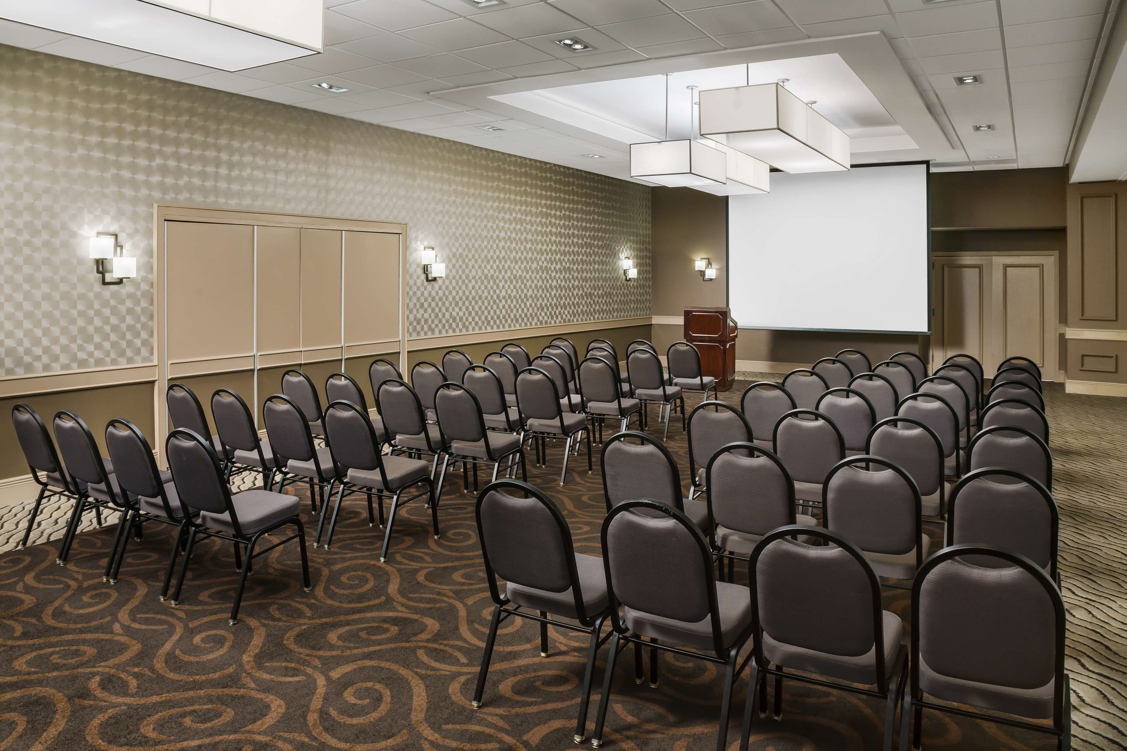 Un salón de conferencias con filas de sillas, un atril y una pantalla de proyección.