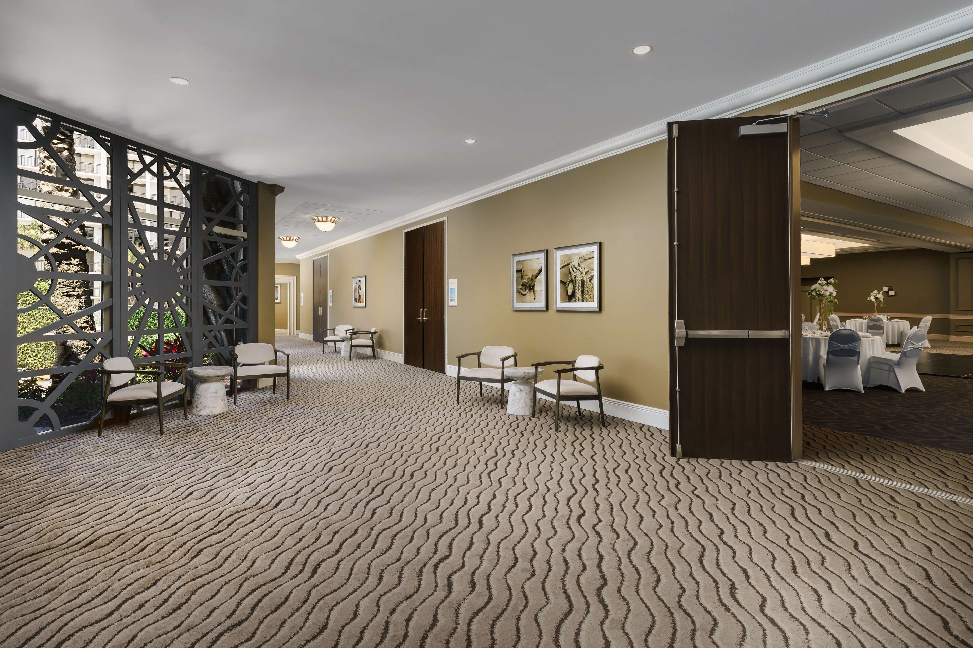 Une pièce spacieuse avec un tapis à motifs, un coin salon avec des fauteuils, une porte en bois et des tableaux encadrés accrochés au mur.