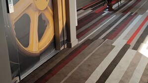 A room with a large yellow wheel, a blue chair, and a striped carpet. - ibis Moulins Sud (Moulins)