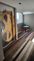 Una habitación con una rueda amarilla grande, una silla azul y una alfombra a rayas.