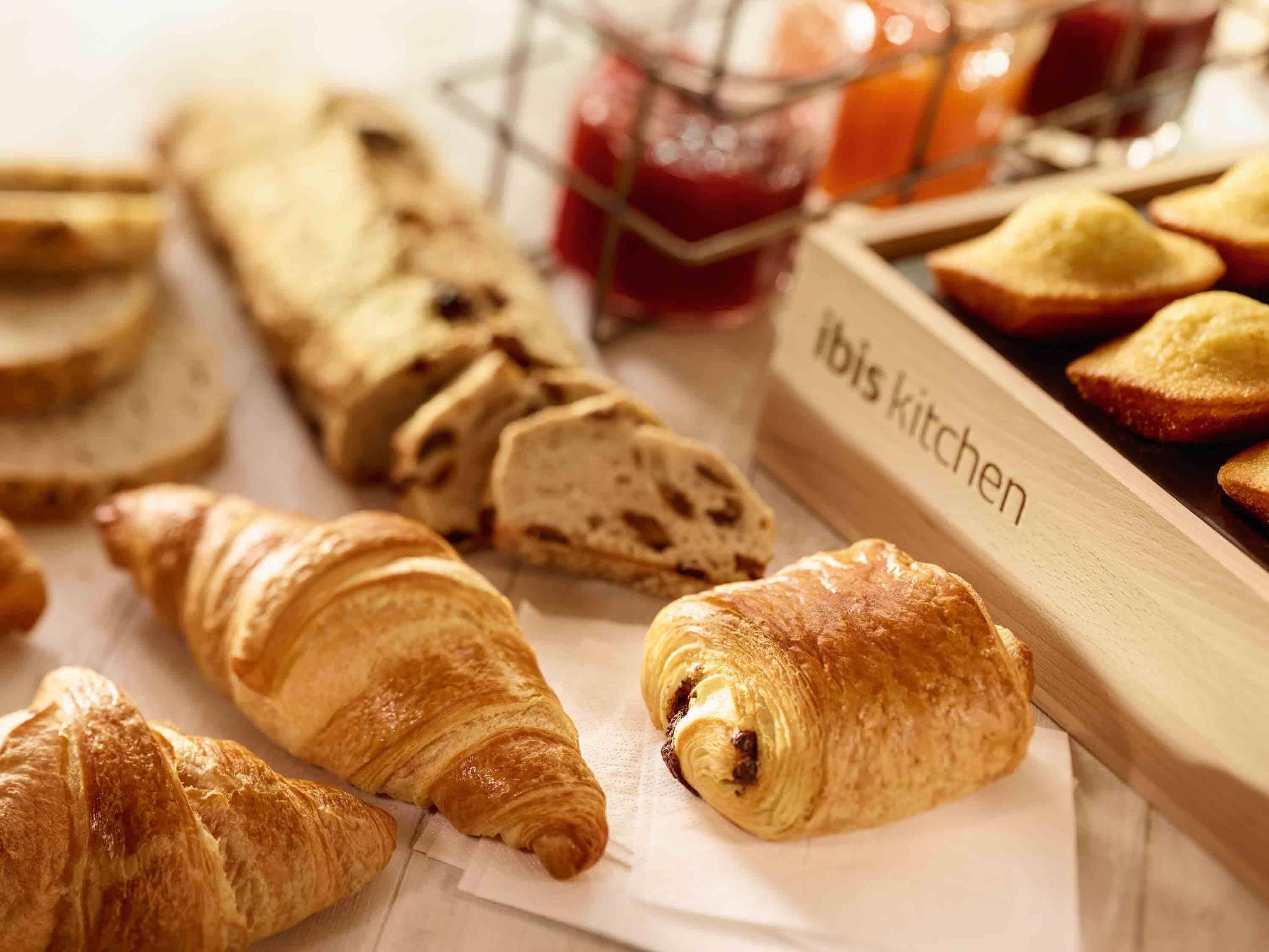 Variedad de productos horneados, como croissants y pan, con un rótulo que dice 'ibis kitchen'.