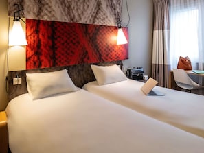 A hotel room with a large bed, two bedside lamps, a desk with a laptop, a chair, and a handbag.