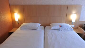A hotel room with two single beds, each with a pillow and a nightstand.