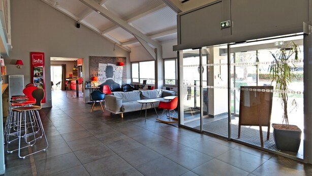 A spacious lobby with a modern design, featuring a seating area with a sofa and chairs, a small table, and a potted plant. - ibis Moulins Sud (Moulins)