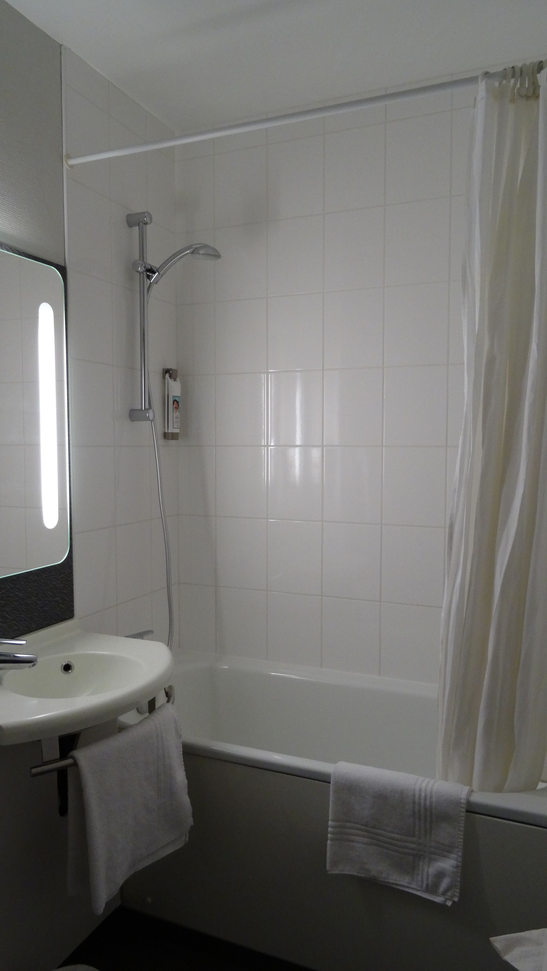 A bathroom with a white sink, mirror, and shower. There are towels hanging on the wall.