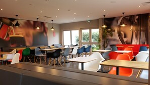 A modern restaurant with booths and tables, large windows, and a mural on the wall. - ibis Moulins Sud (Moulins)