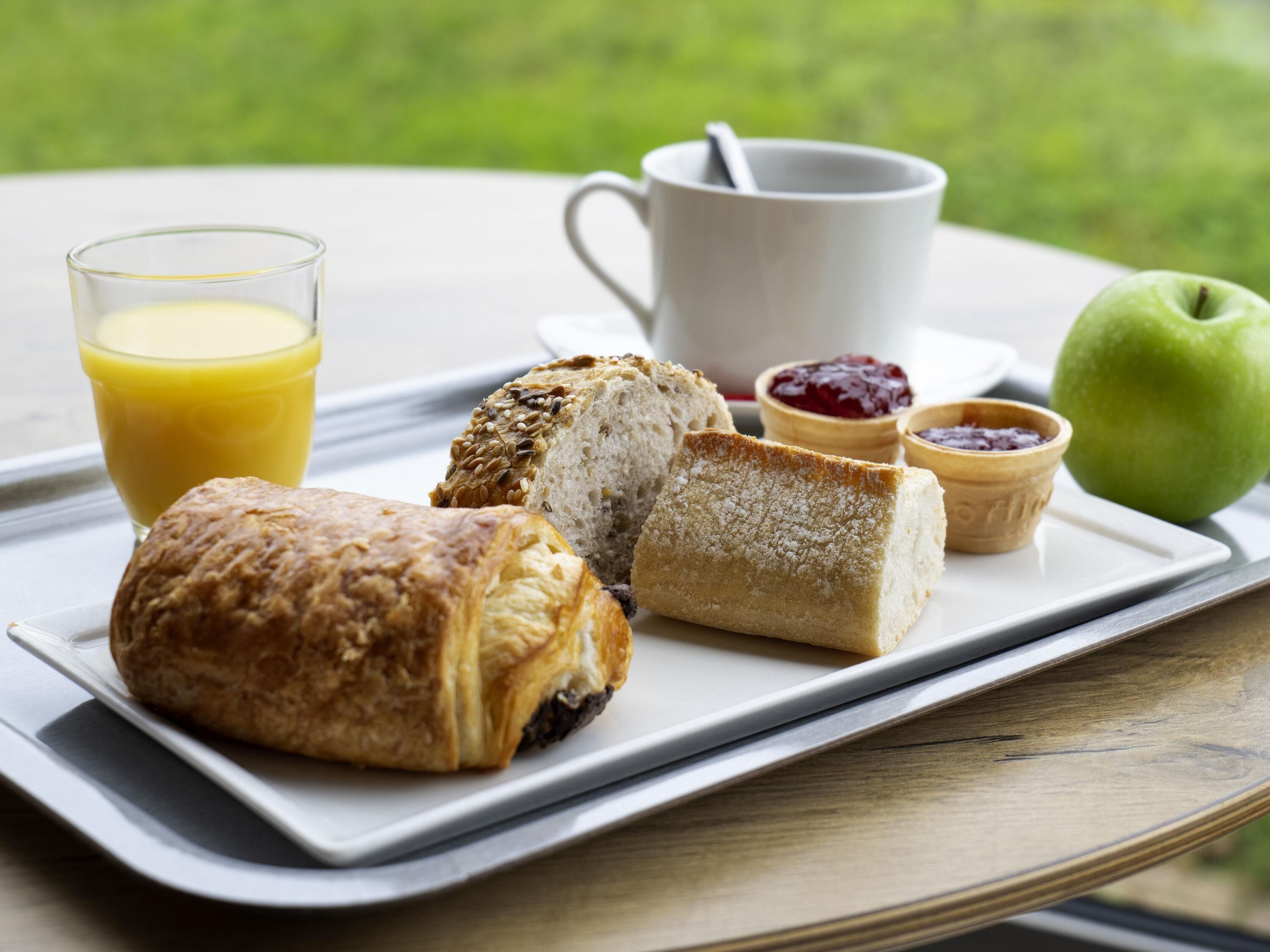 A breakfast tray with pastries, a glass of orange juice, a cup, jam, and an apple on a table.