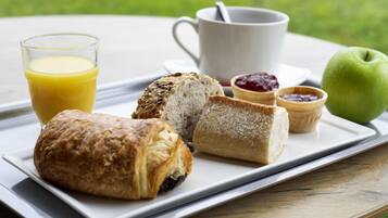 A breakfast tray with pastries, a glass of orange juice, a cup, jam, and an apple on a table.