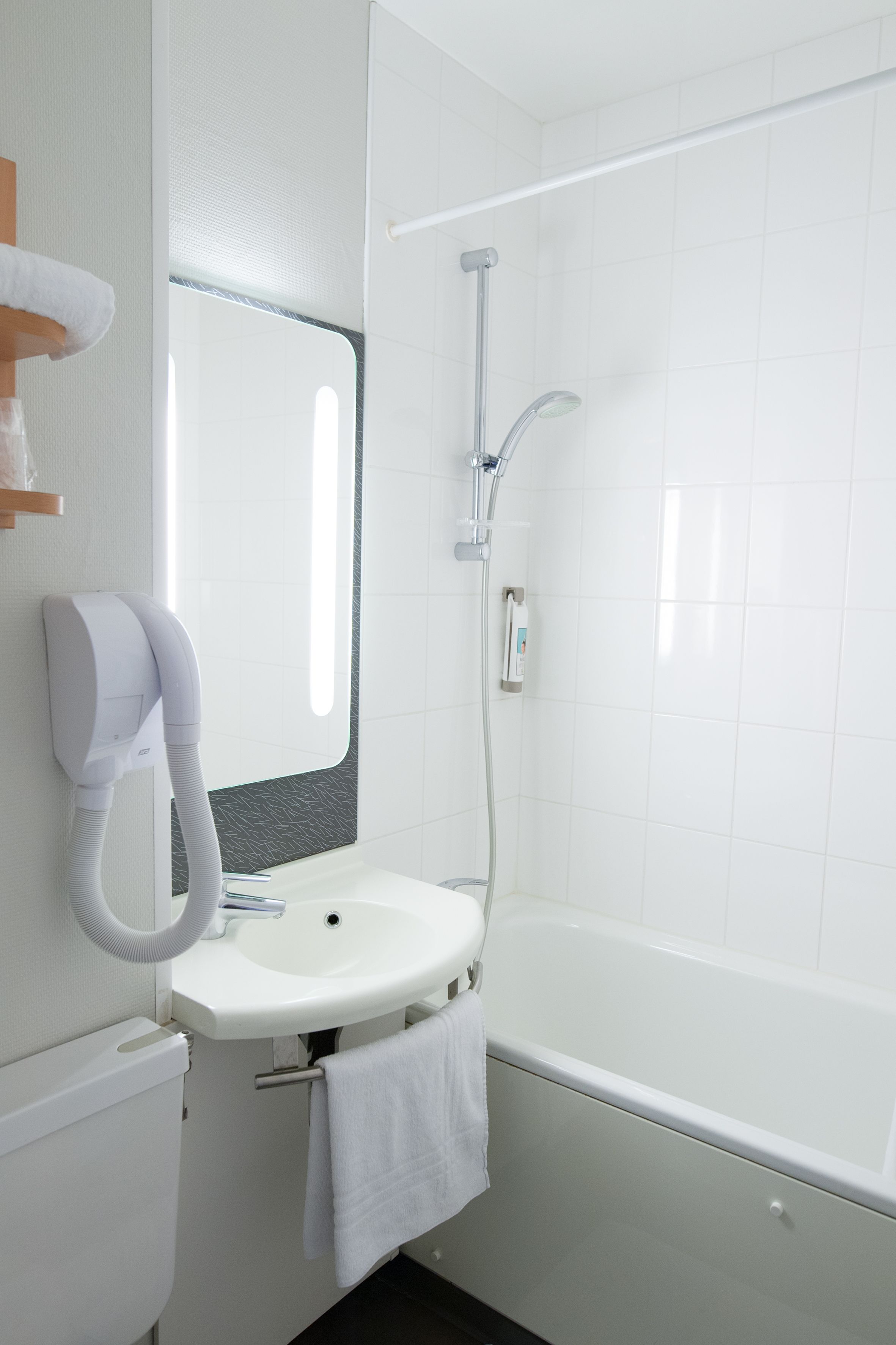 Uma casa de banho moderna com uma pia branca, um espelho, um secador de cabelo portátil e um chuveiro.