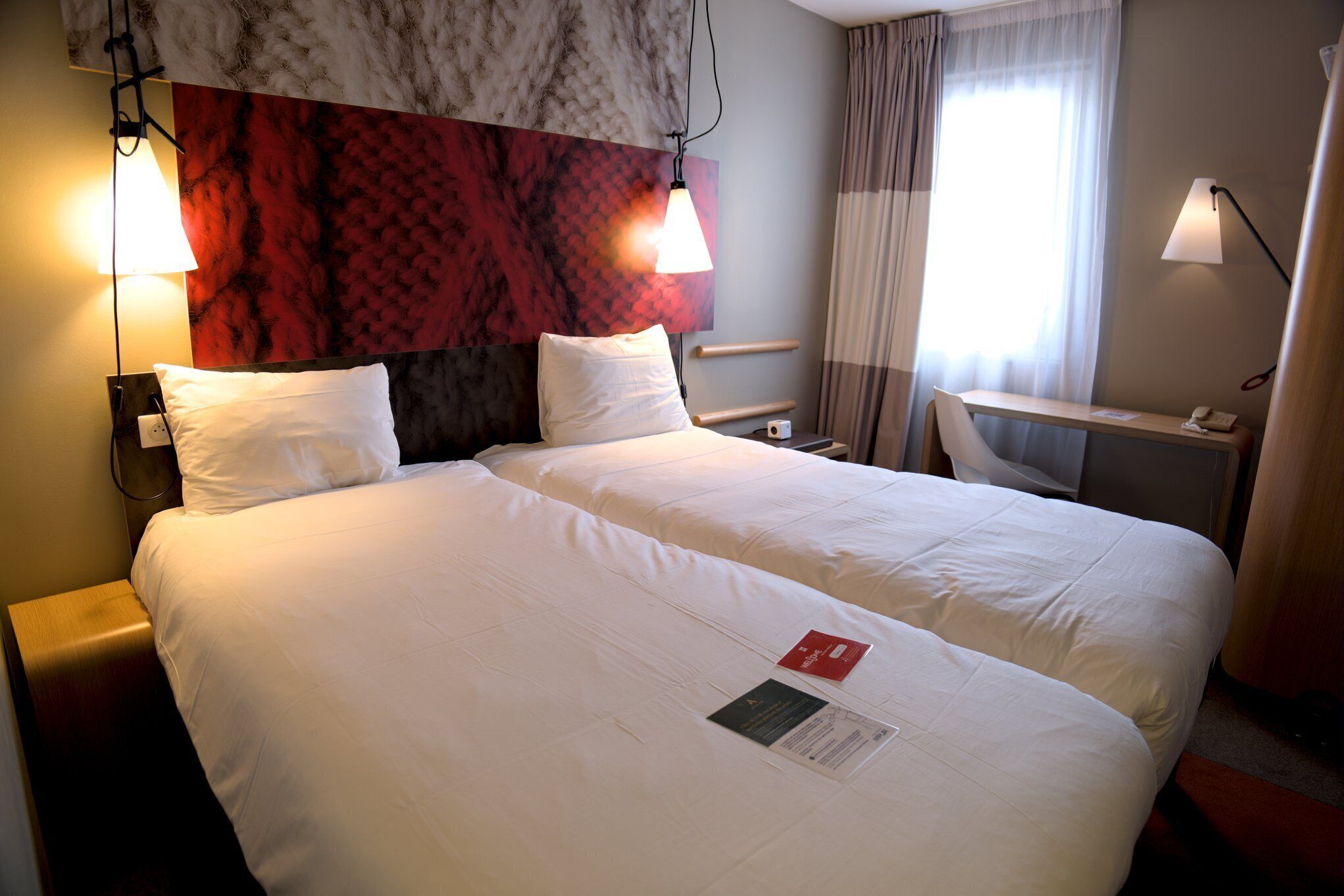 A hotel room with a large bed, two bedside lamps, a desk, and a window with curtains.