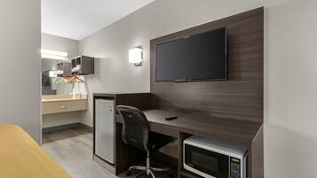 Une chambre d’hôtel compacte comprenant un coin cuisine, un téléviseur à écran plat fixé au mur, un bureau avec une chaise et un four à micro-ondes.