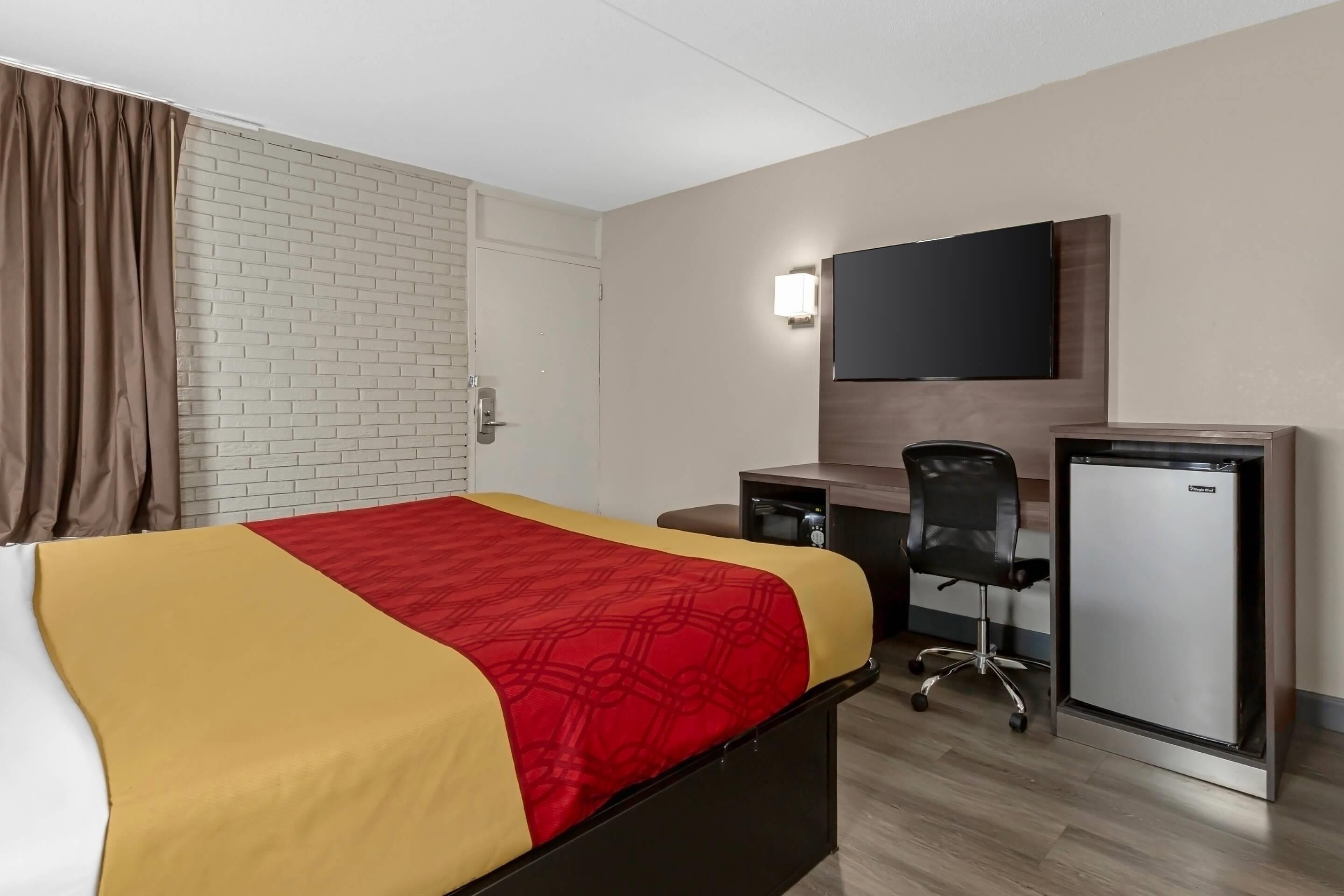 A hotel room with a bed, desk, chair, and a small refrigerator.