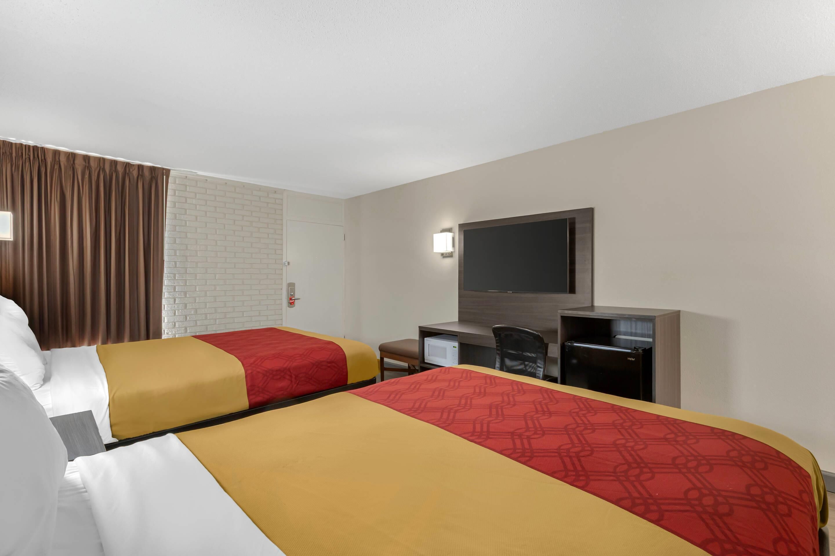 Een hotelkamer met twee bedden, een bureau, een stoel, een televisie en een witte bakstenen muur.
