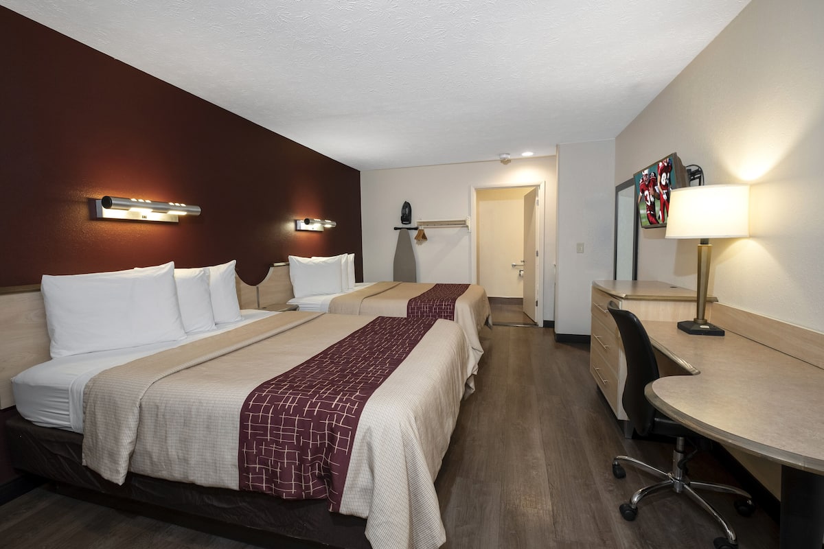 A hotel room with two beds, a desk, a chair, a lamp, and a mirror.