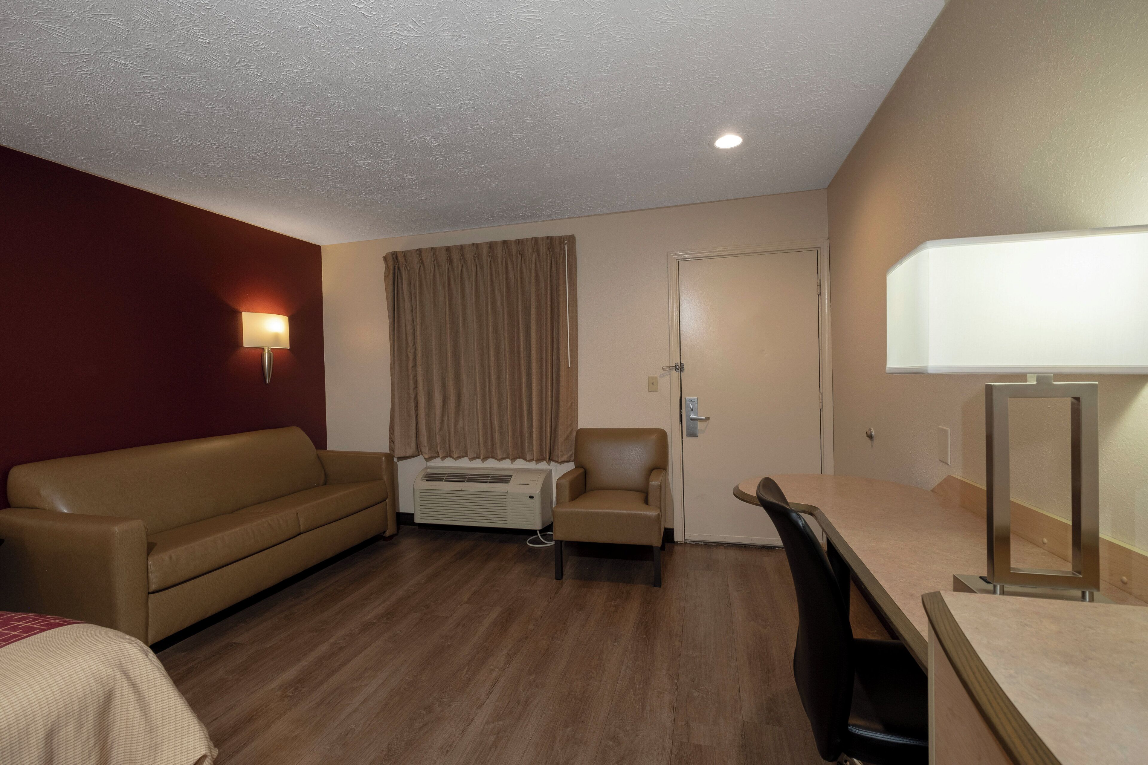 A hotel room with a sofa, a chair, a desk, and a lamp.