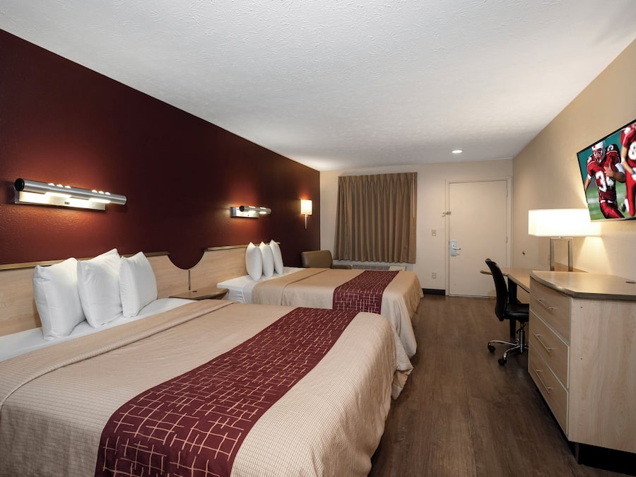 A hotel room with two beds, a desk, a chair, a TV, and a lamp.