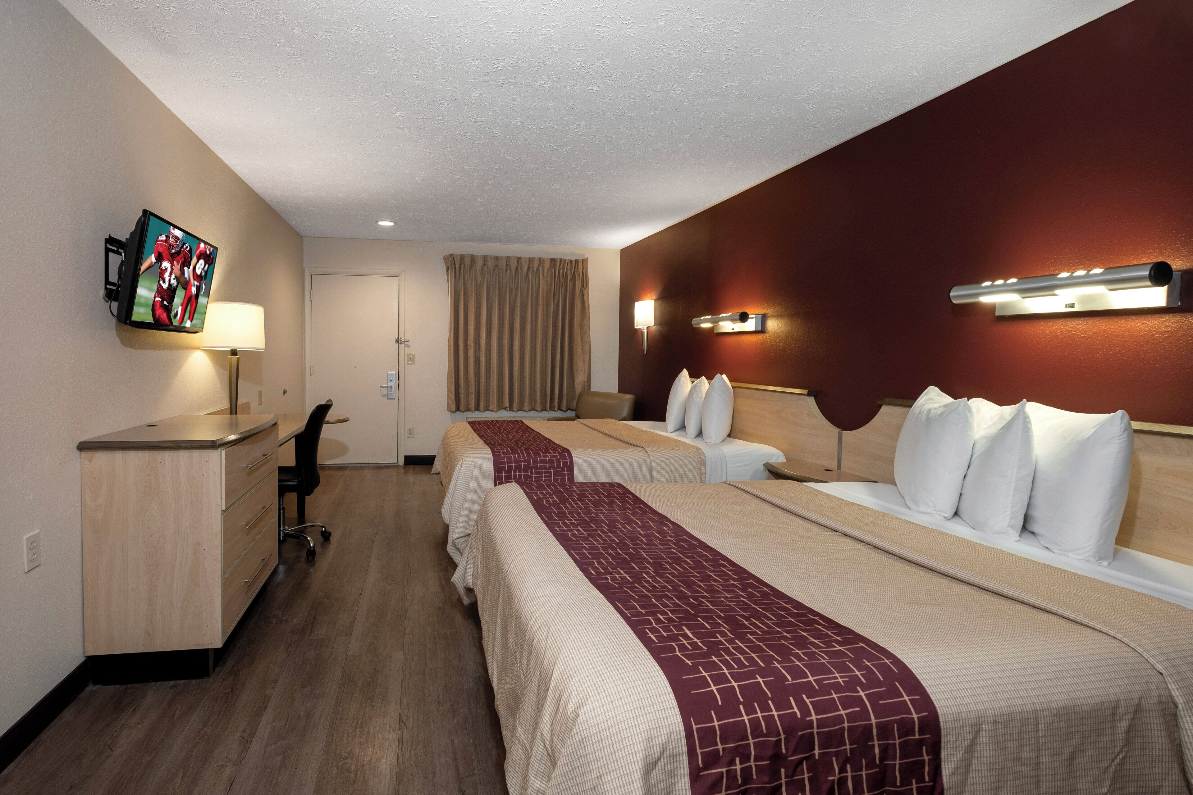 A hotel room with two beds, a desk, a TV, and a bathroom door.