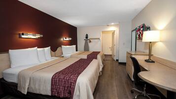 Una habitación de hotel con dos camas, un escritorio, una silla, un televisor y una lámpara.