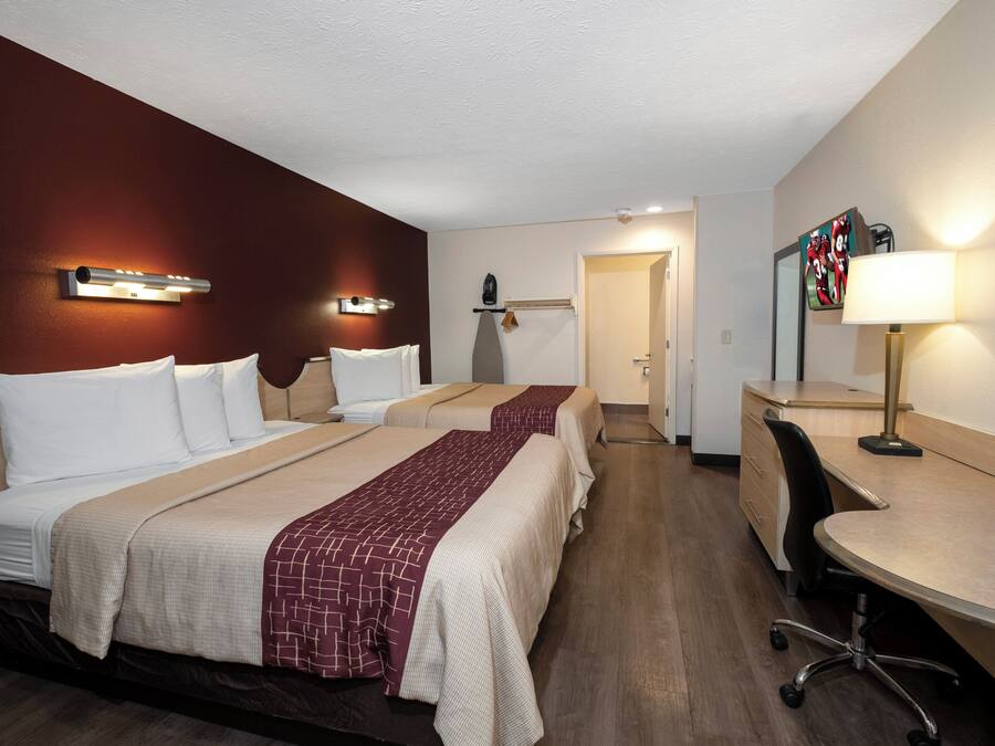 Una habitación de hotel con dos camas, un escritorio, una silla, un televisor y una lámpara.