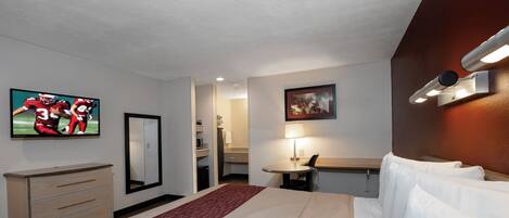 Una habitación de hotel con cama, escritorio, televisión, espejo y puerta que da a un baño.