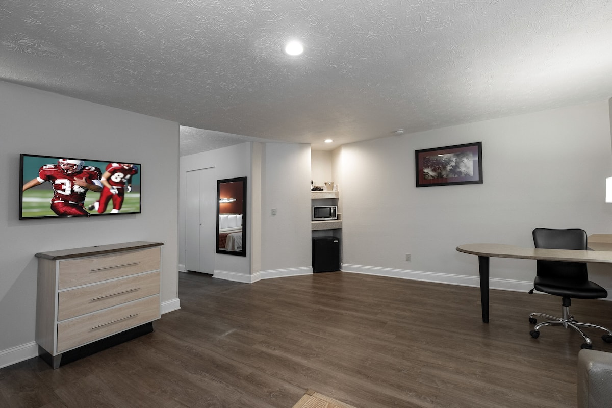 A spacious room with a wooden floor, a desk, a chair, a television, and a microwave.