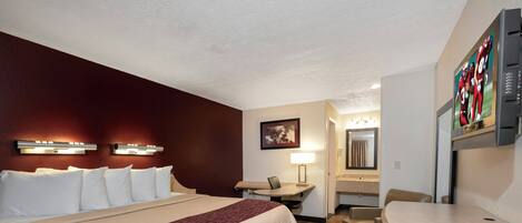 A hotel room with a large bed, a desk, a chair, a mirror, and a television.